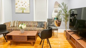 A modern living room with a sofa, two armchairs, a coffee table, and a TV. - 85a Charming, Cozy 3BR, 2BA Home Near Downtown Boston (Boston)