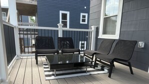 A deck with a glass-top table and two black chairs, a striped rug, and a railing. - 85a Charming, Cozy 3BR, 2BA Home Near Downtown Boston (Boston)