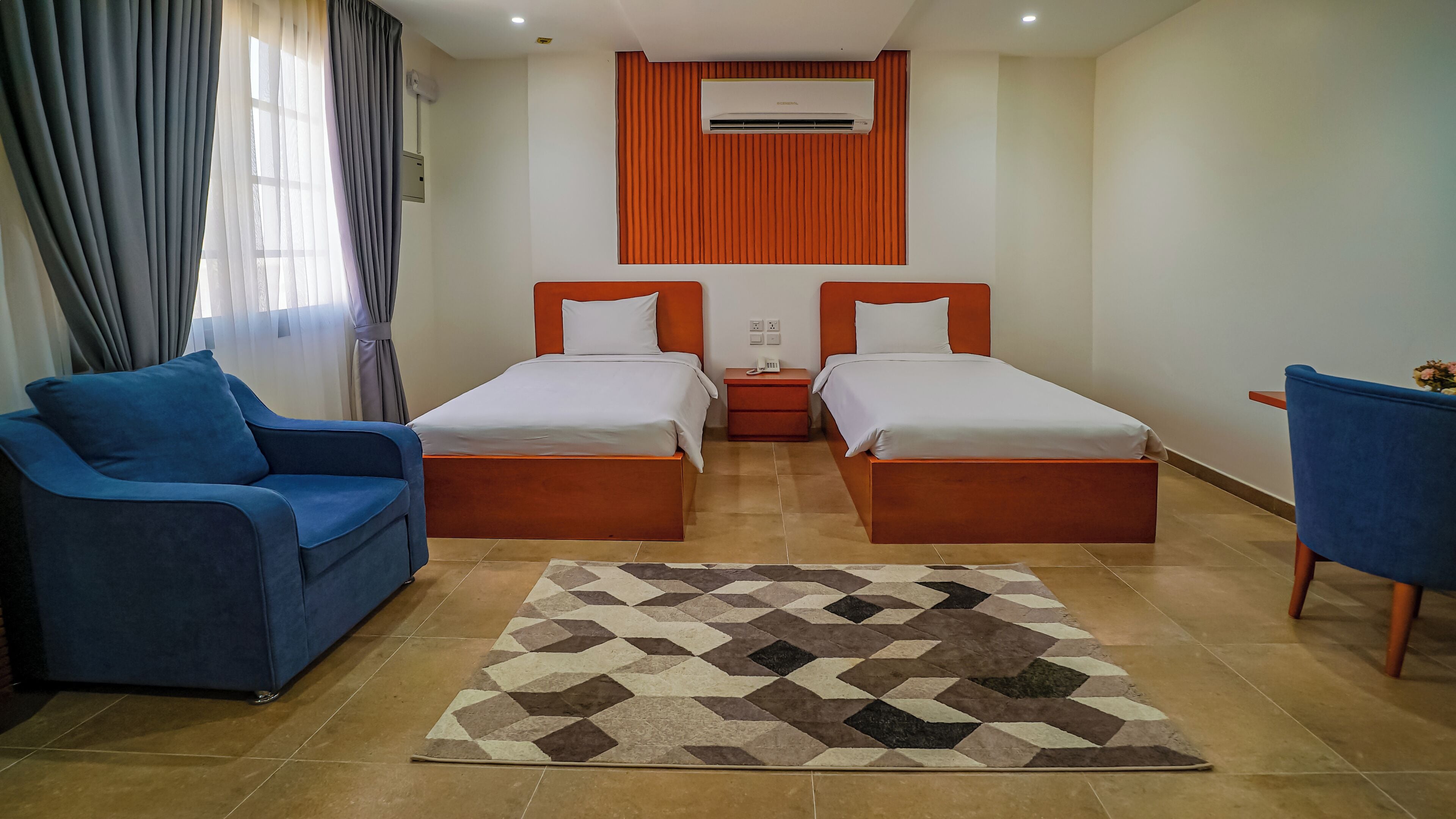 Camera d'albergo con due letti, un divano blu, un tappeto decorato e un condizionatore d'aria.