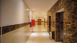 A hotel corridor with marble walls, a fire extinguisher, a trash bin, and a door at the end.