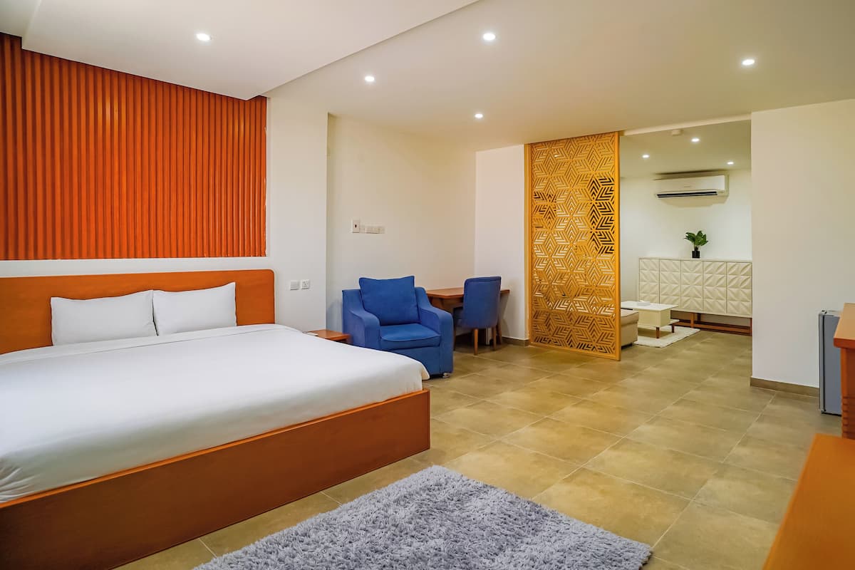 A hotel room with a large bed, a desk, a chair, and a small table.
