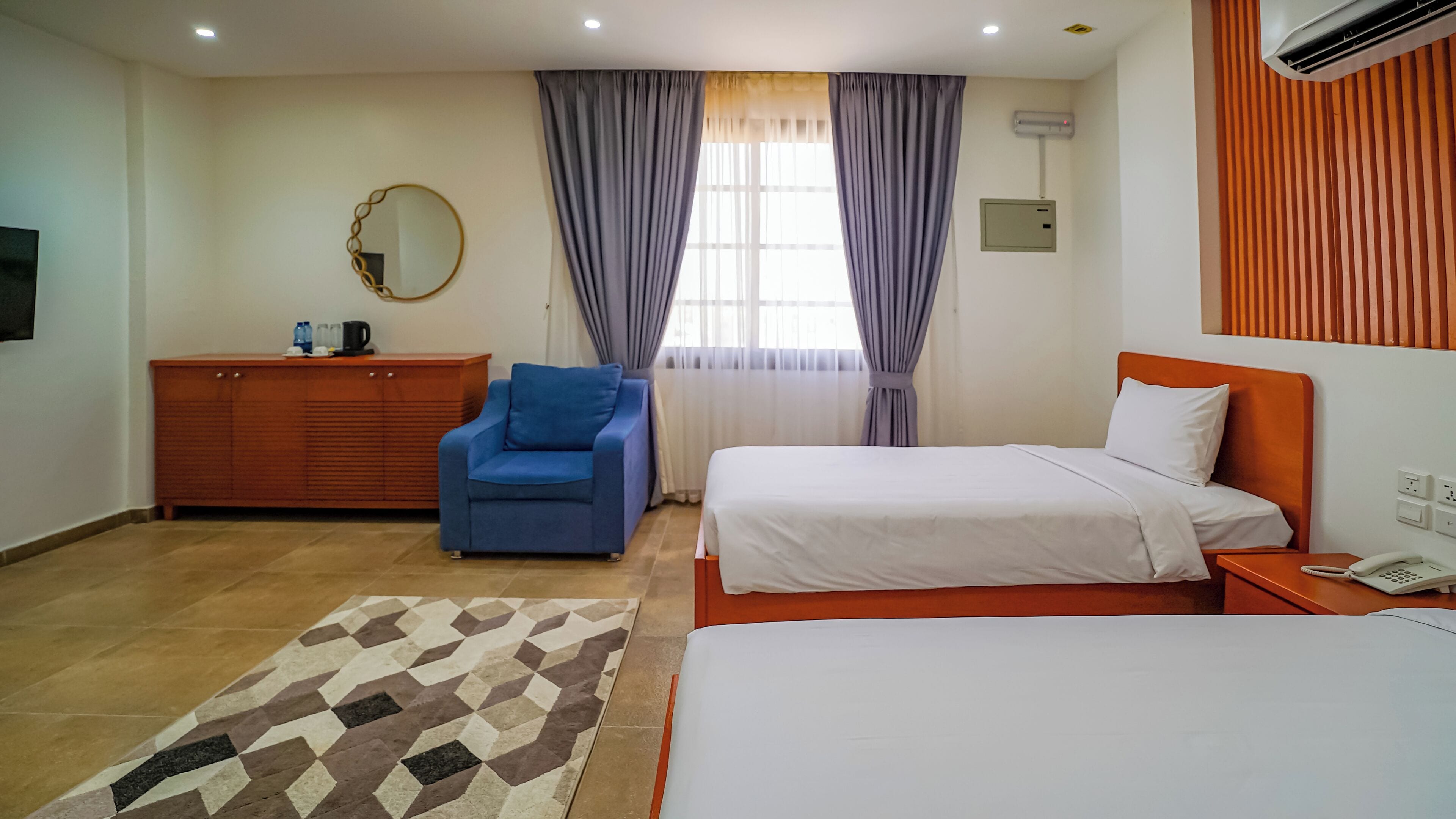 Une chambre d’hôtel avec un lit, un canapé, une commode, un miroir et une fenêtre avec des rideaux.