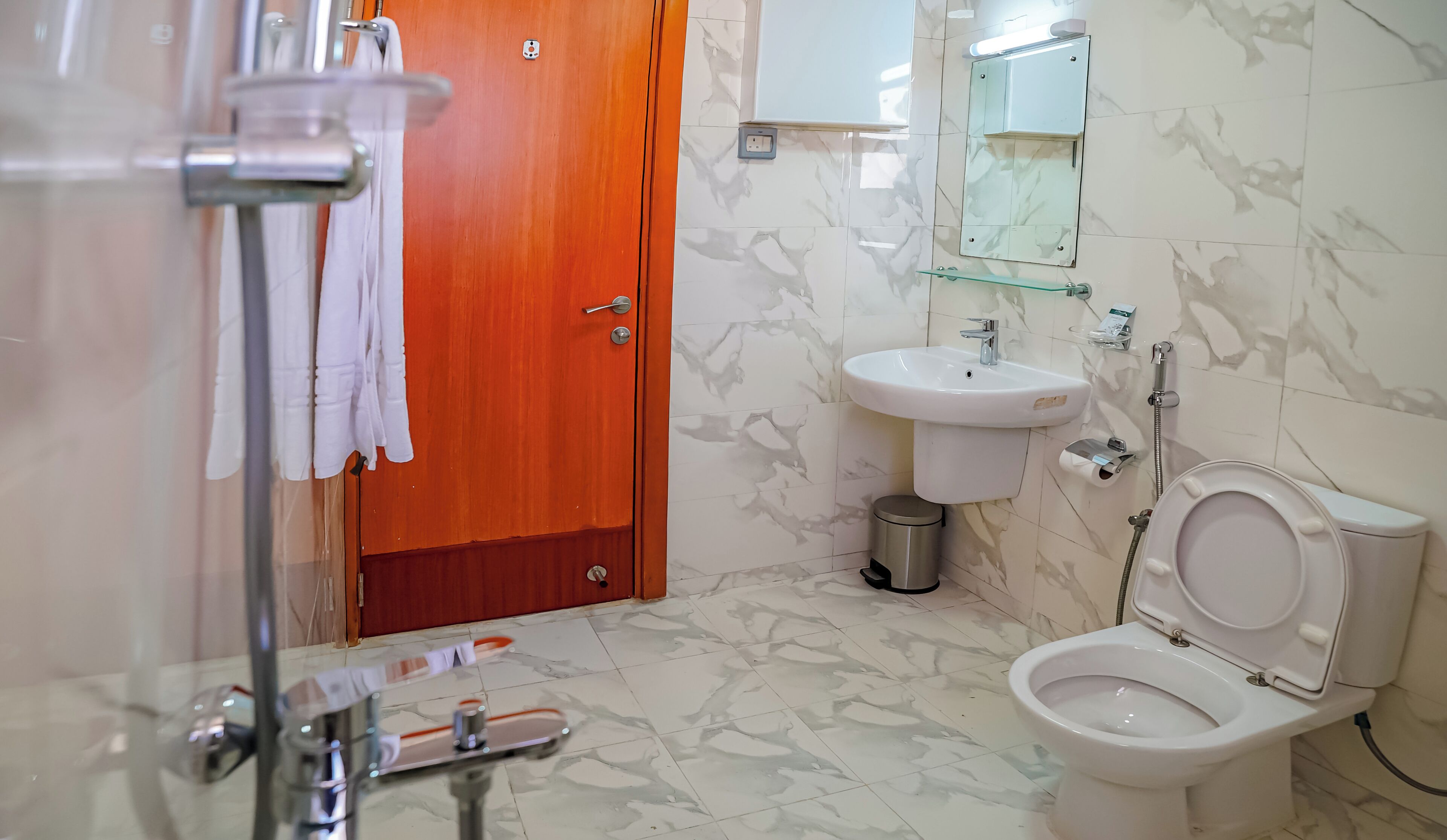 A bathroom with a wooden door, a white sink, a mirror, and a toilet.