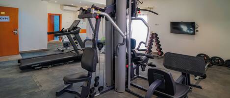Un gimnasio con equipamiento de ejercicio, una cinta de correr y una banca.