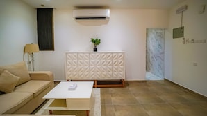 A modern living room with a beige sofa, a white coffee table, a decorative cabinet, an air conditioning unit, and a potted plant.