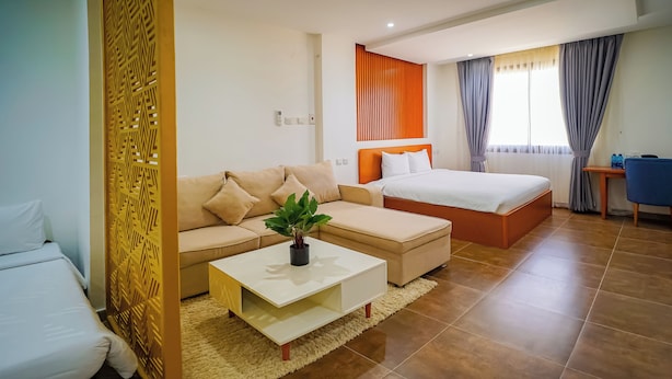 A modern hotel room with a sofa, a bed, a coffee table, and a small desk.