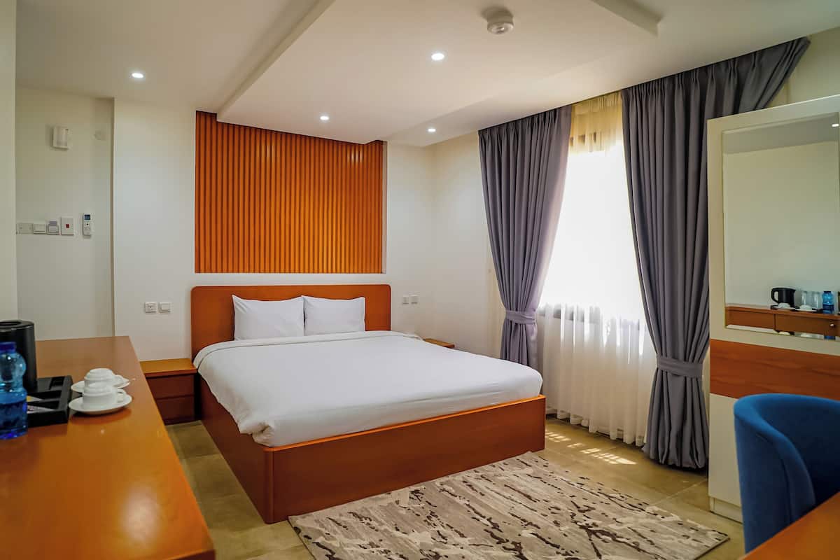 A hotel room with a bed, a desk with water bottles, a coffee maker, and a mirror.