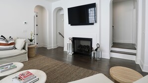 Una sala de estar moderna con chimenea, un televisor de pantalla plana montado encima y una escalera que sube a un nivel superior.