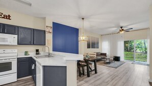A modern kitchen with dark cabinets, a white countertop, and a dining area with a table and chairs. - Last Minute Disney Getaway! Private Pool & Themed Bedrooms. Book Now! #121909 (Orlando)