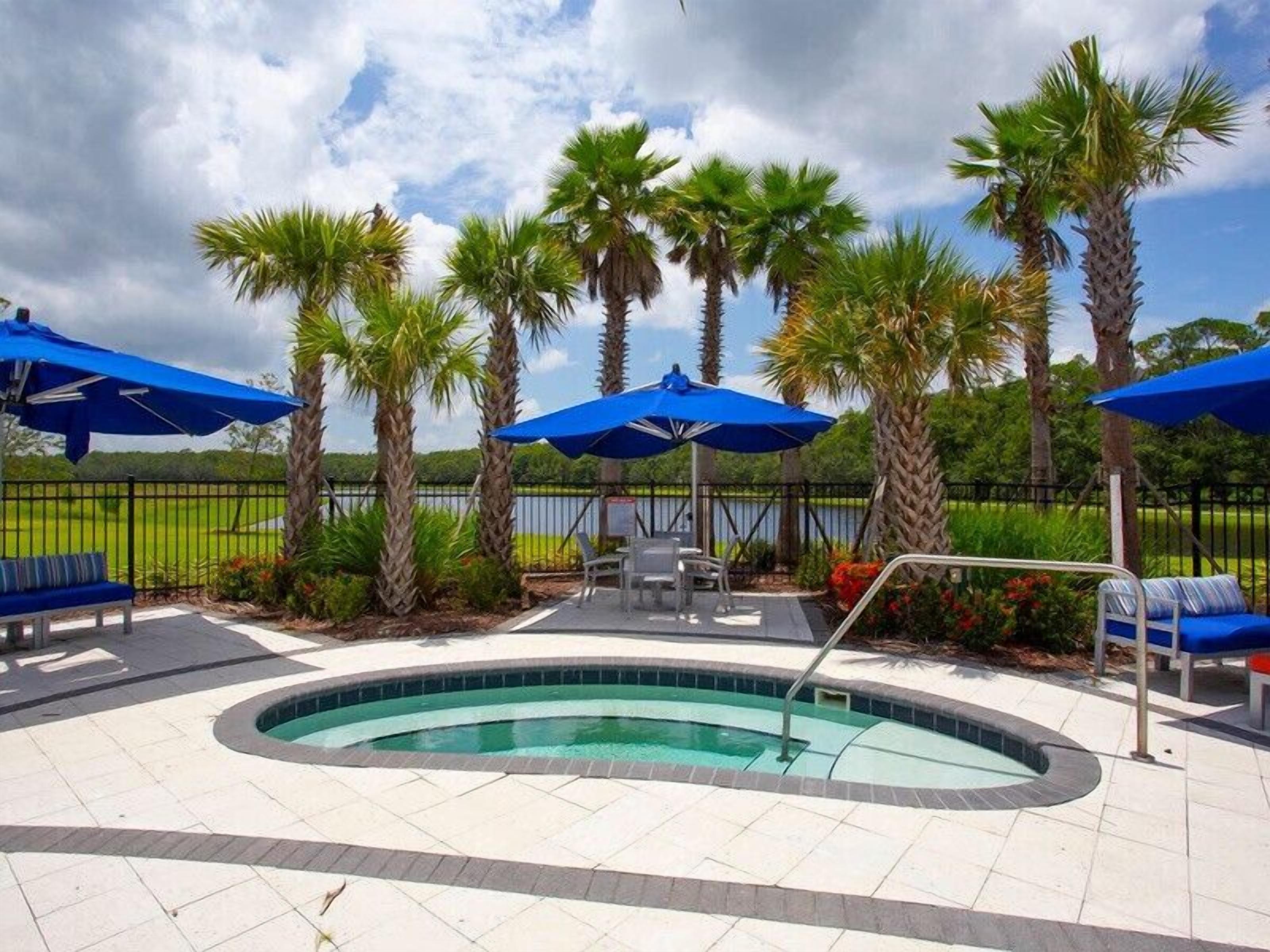 A pool area with blue umbrellas, lounge chairs, and palm trees.