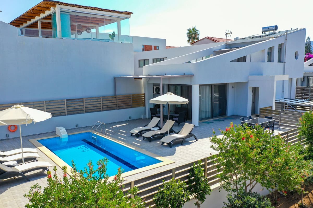 A modern outdoor pool area with a clear blue pool, sun loungers, and a covered seating area.