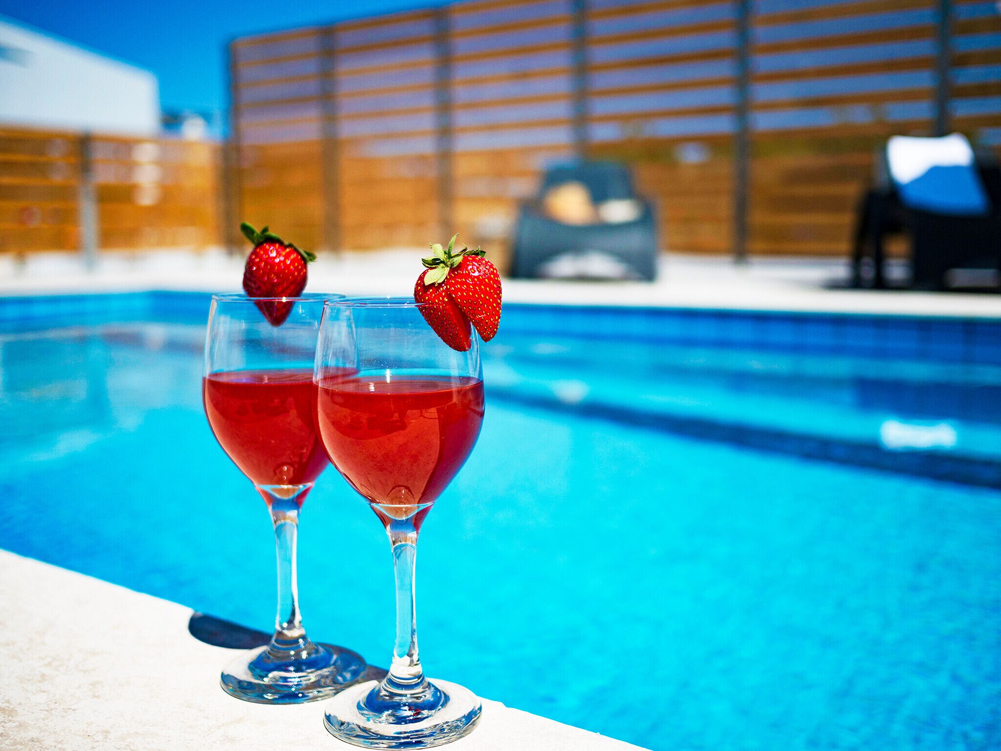 Duas taças de bebida vermelha com morangos à beira da piscina.