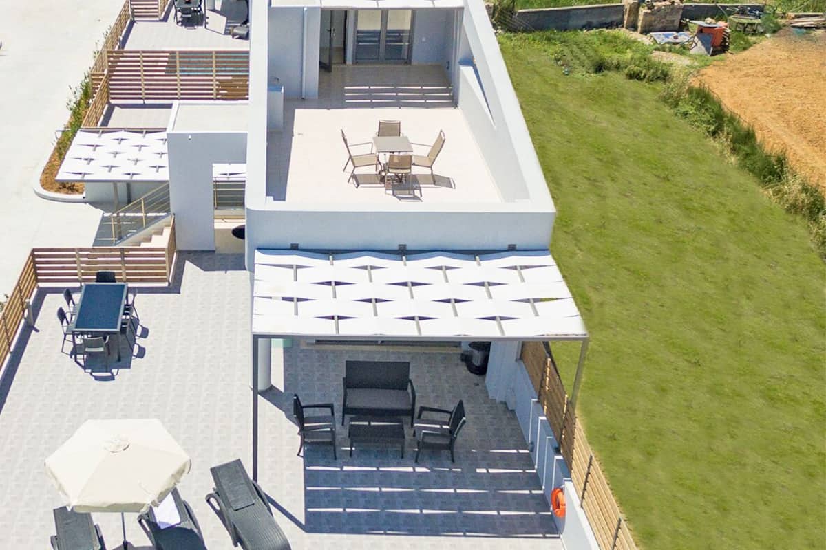 A rooftop pool area with a blue pool, sun loungers, a table with chairs, and a covered seating area.