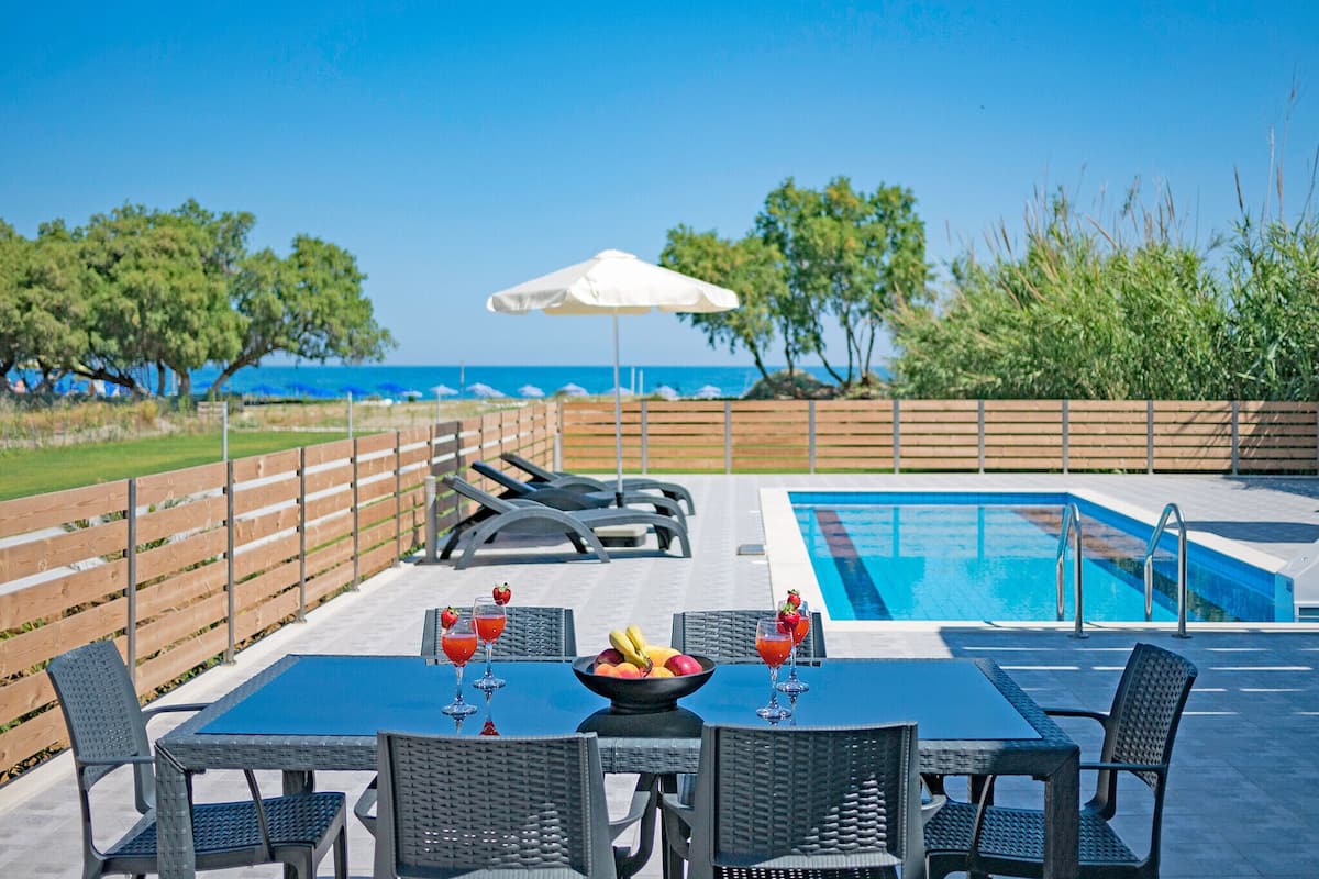 An outdoor seating area with a pool, tables, chairs, and a view of the sea.