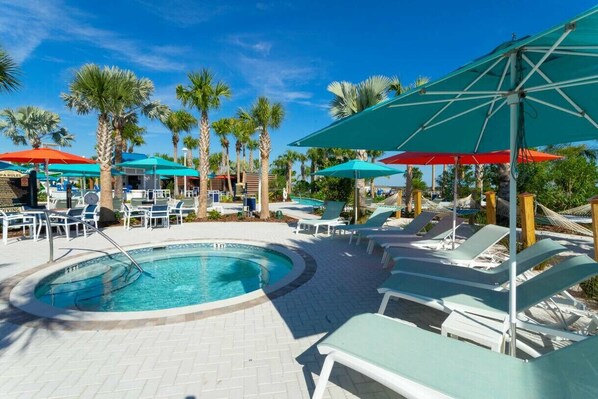 A pool area with lounge chairs and umbrellas, surrounded by palm trees.