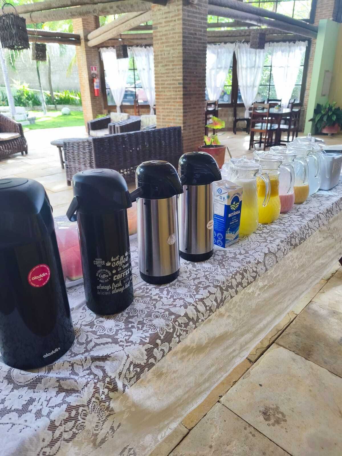 A coffee station with kettles and a coffee machine, a lace tablecloth, and a view of the outdoor seating area.