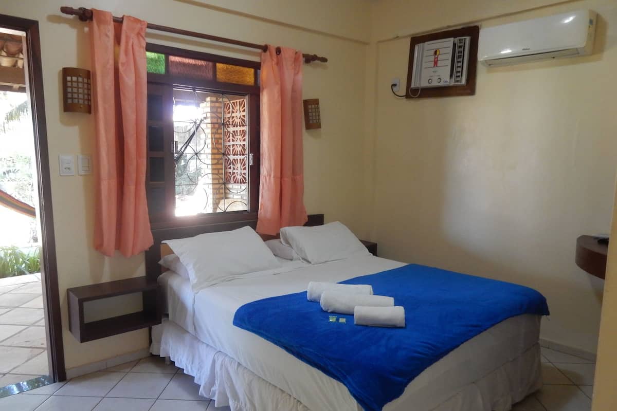 Een hotelkamer met een bed, gordijnen, een airconditioning en een raam met decoratief zonnescherm.