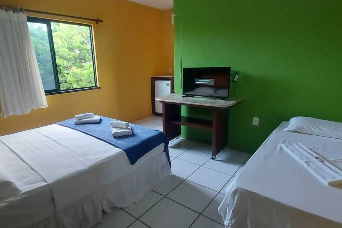 Een kamer met twee bedden, een televisie op een standaard, een raam met gordijnen en een groene wand.