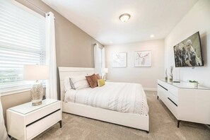 Un dormitorio con cama, mesitas de noche, cómoda y televisor en la pared.