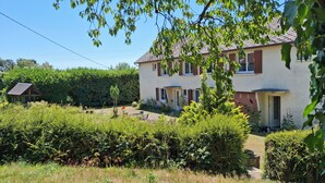 Una casa a due piani con un giardino antistante, un piccolo deposito e un cielo azzurro limpido.