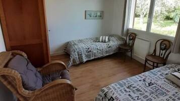 Un dormitorio con una cama, dos sillas, un sillón de mimbre, una lámpara colgante, una ventana y una puerta.