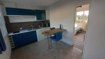 A compact kitchen with blue cabinets, a wooden table, and a blue chair.