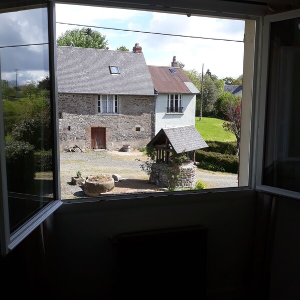 Une maison en pierre avec une partie supérieure blanche et un petit jardin visible à travers une fenêtre.