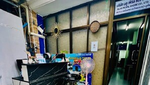 A reception area with a black marble counter, a black leather sofa, a small fan, and a poster advertising travel and tours. - Blue Pearl Shore (Patong)