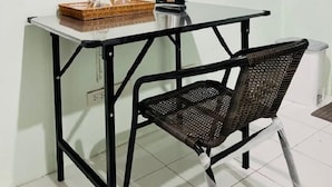 A small room with a TV mounted on the wall, a table with a kettle and a basket, and a wicker chair. - Blue Pearl Shore (Patong)