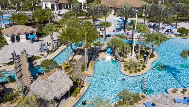 Un complexe hôtelier doté d’une grande piscine, de palmiers et d’un chalet à toit de chaume.
