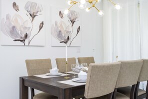 Een eethoek met een donker houten tafel, beiges beklede stoelen en een moderne kroonluchter.