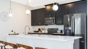 Une cuisine moderne avec des meubles de couleur sombre, des appareils en acier inoxydable et un îlot central blanc doté de tabourets de bar.