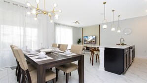 Un espace repas moderne avec une table en bois foncé, des chaises recouvertes d’un tissu beige et un lustre.