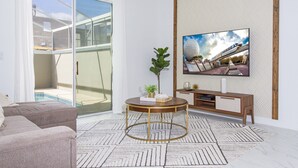 Un salon moderne doté d’une porte vitrée donnant sur un balcon, d’une table basse ronde, d’un téléviseur fixé au mur et d’un tapis à motifs.