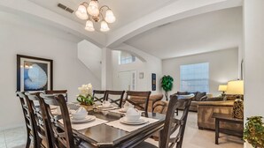 A dining area with a dark wooden table set for four, surrounded by matching chairs. A staircase leads to an upper level. - Last Minute Disney Getaway! Private Pool, Hot Tub & Game Room. Book Now! #65763 (Orlando)