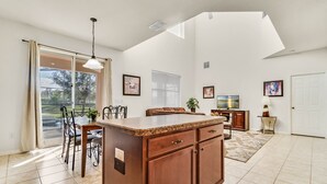 A spacious kitchen with a large island, a dining area with chairs, a sliding glass door to the outdoors, and a small side table with a lamp. - Last Minute Disney Getaway! Private Pool, Hot Tub & Game Room. Book Now! #65763 (Orlando)