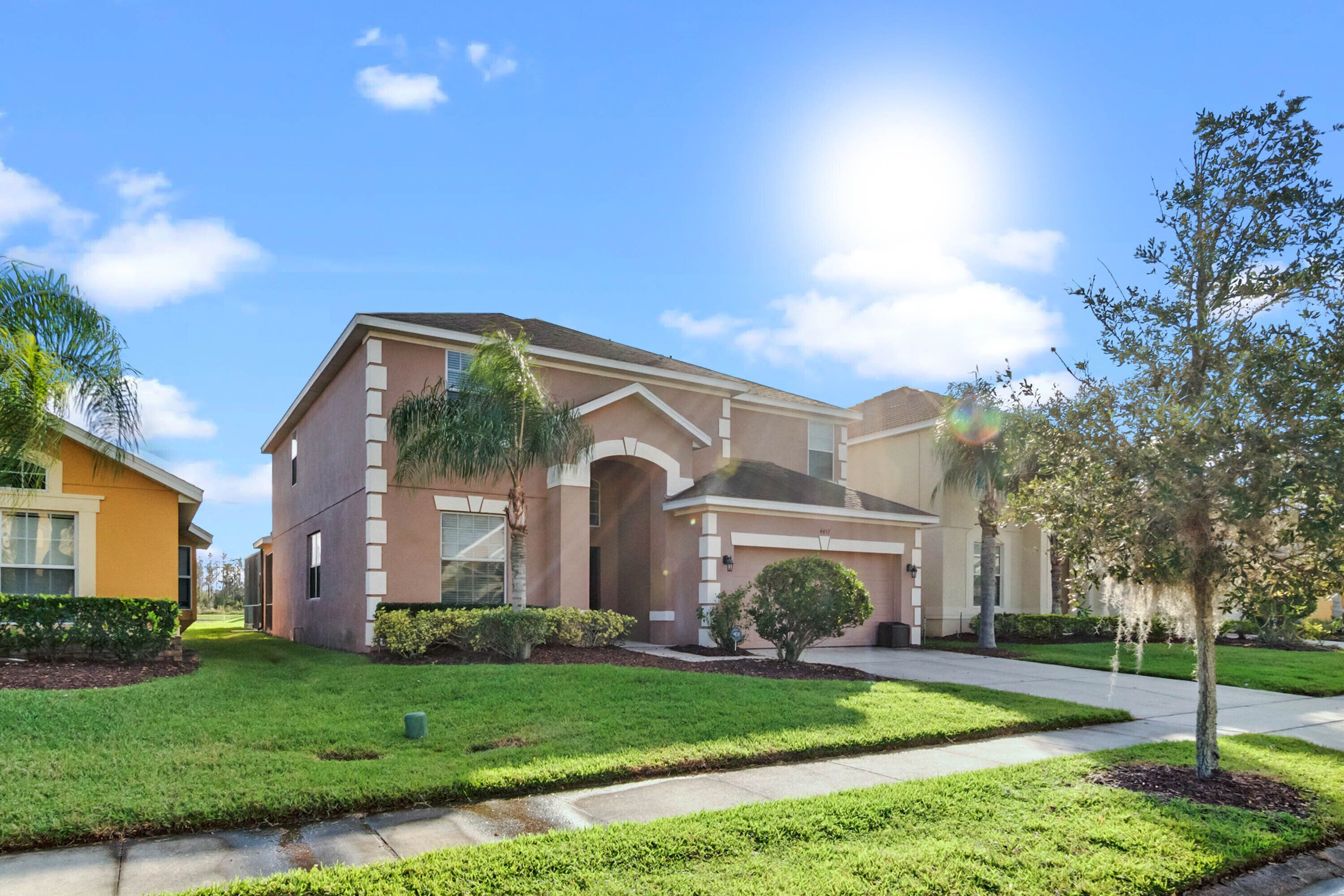 A two-story residential house with a front yard, driveway, and a small tree.
