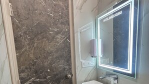 Een badkamer met een marmeren wastafel, een wastafel, een spiegel met LED-verlichting en een deur met een marmeren afwerking.