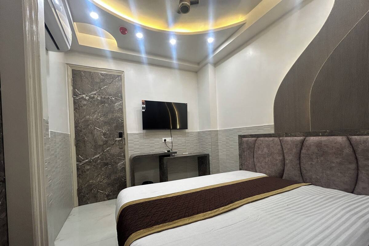 A modern hotel room with a large bed, a vanity with a mirror, and a flat-screen TV mounted on the wall.