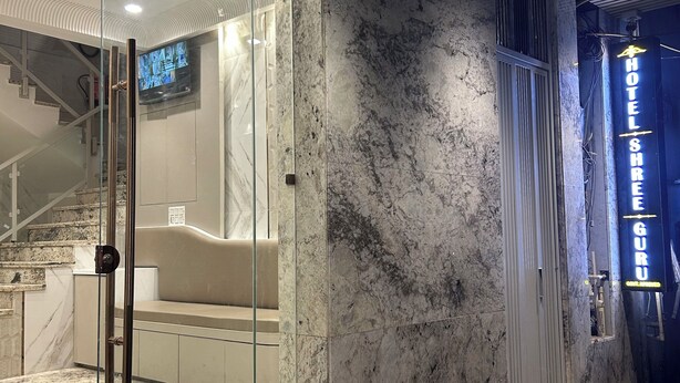 Een modern hotelinterieur met een glazen douchecabine, marmeren wanden en een trap naar een zithoek.