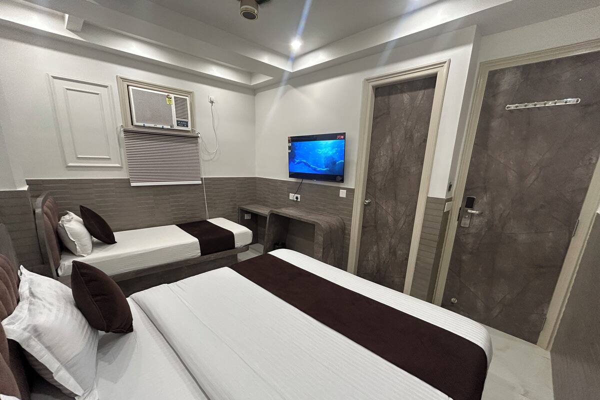 A hotel room with two beds, a TV, a door, and a window with blinds.