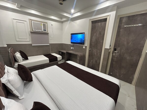 A hotel room with two beds, a TV, a door, and a window with blinds. - Hotel Shree Guru (New Delhi)