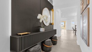 A modern hallway with a dark wall, a round mirror, a vase with white flowers, and a wooden tray. There are three grey ottomans with orange handles. - Last Minute Disney Getaway! Private Pool, Hot Tub & Game Room. Book Now! #118999 (Orlando)