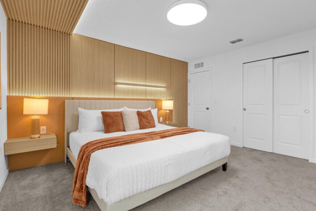 Un dormitorio con cama, lámparas de noche, cabecera de madera y armario.