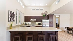 Une cuisine moderne dotée d’un grand îlot central, de meubles en bois foncé, d’appareils électroménagers en acier inoxydable et offrant une vue sur la salle à manger.