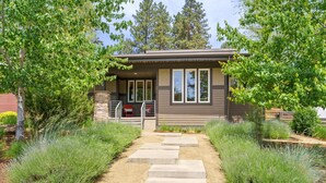 Une maison moderne avec un chemin de pierre menant à l’entrée, entourée d’une végétation luxuriante et d’arbres.