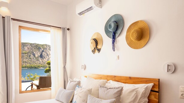 Une chambre avec un lit en bois, une vue sur l’extérieur et deux chapeaux accrochés au mur.