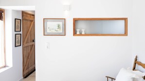 Une pièce avec une porte en bois, un tableau encadré, une étagère ornée d’objets décoratifs et un lit avec une tête de lit en bois.