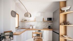 Une cuisine moderne avec des meubles blancs, un plan de travail en bois, un four à micro-ondes et un coin repas comprenant une table blanche et un panier en osier.