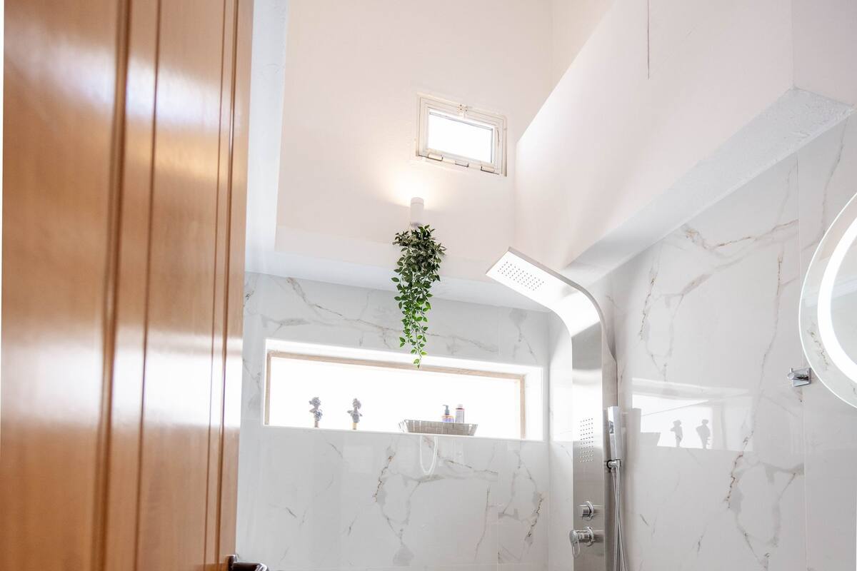 A modern bathroom with a marble wall, a shower, a toilet, and a sink.